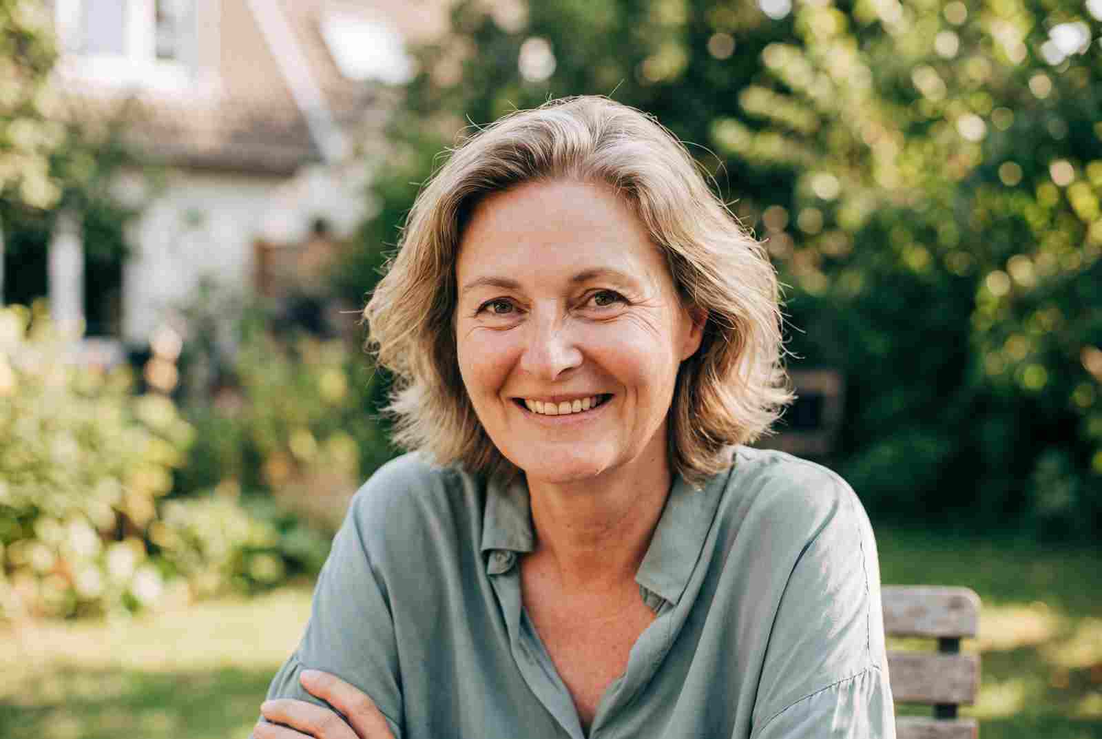 Marion lächelt entspannt im Garten im Tageslicht