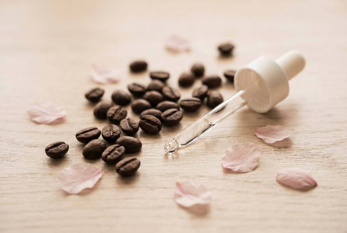 Kaffeebohnen und eine Pipette mit Serum sowie Kirschblütenblätter auf hellem Holz