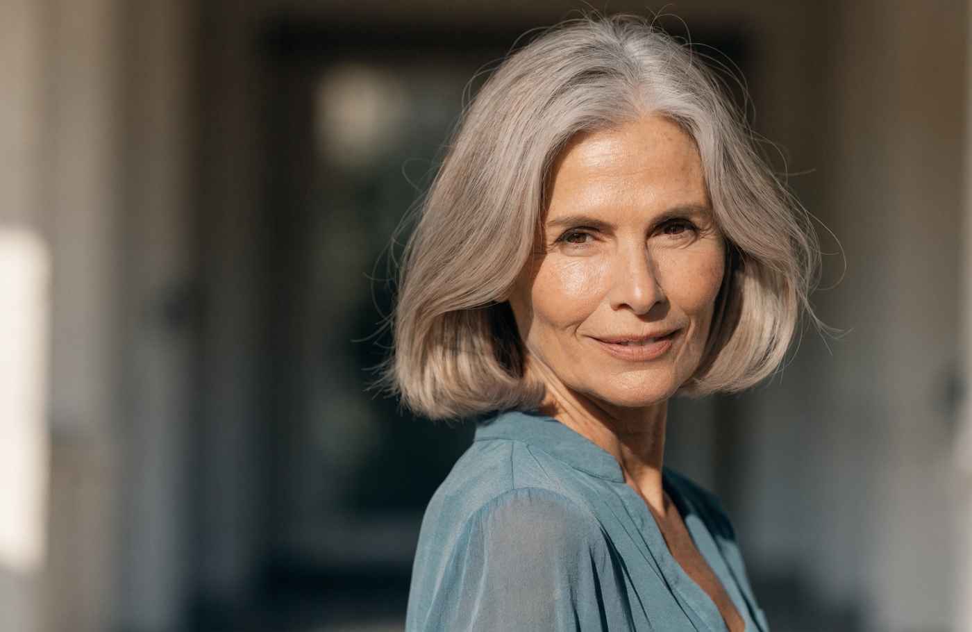 Birgit (57) mit silbergrauem Haar in türkisfarbener Bluse, warmes Tageslicht, Blick in die Kamera