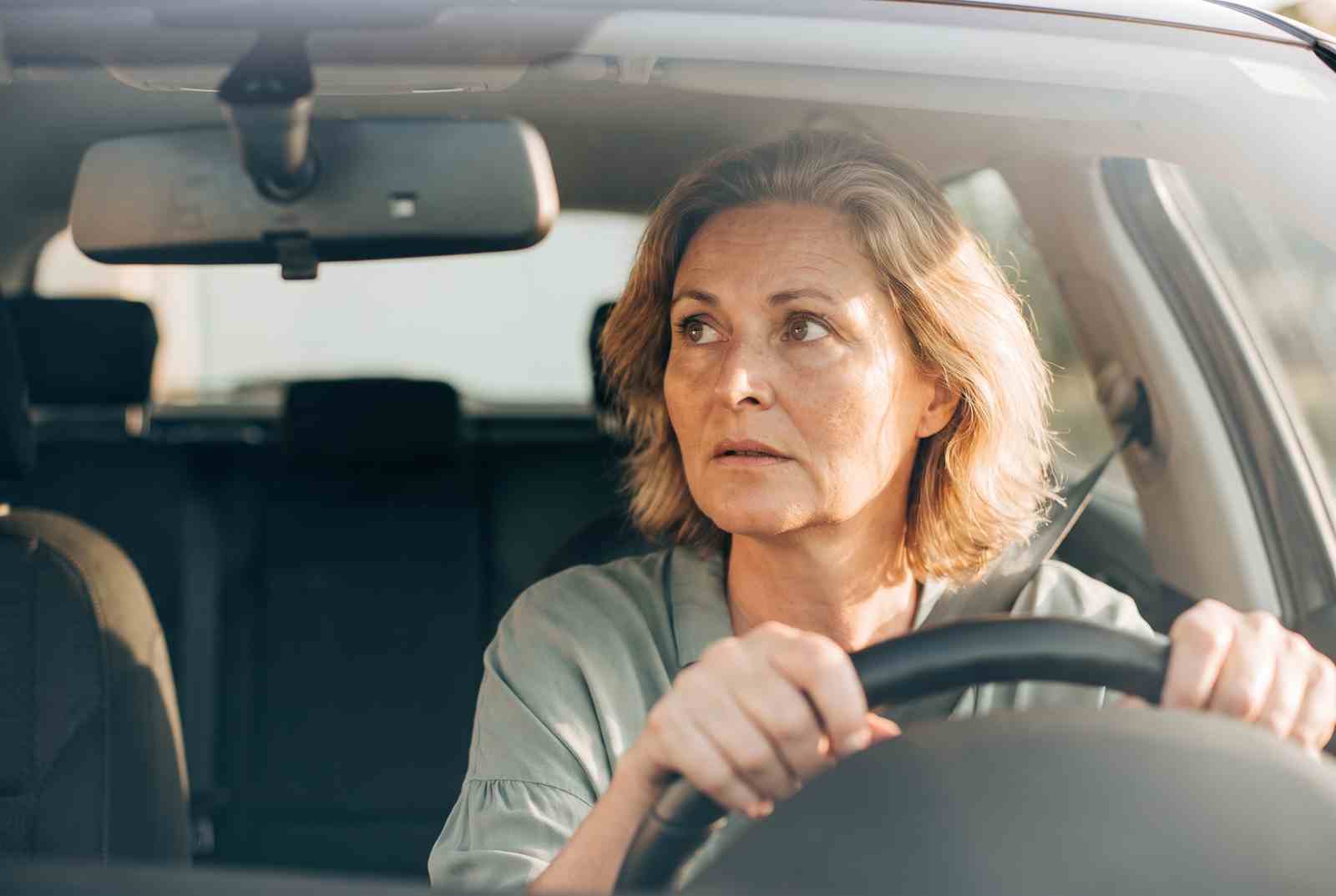 Marion sitzt im Auto und blickt bei Sonnenlicht zur Seite in den Rückspiegel
