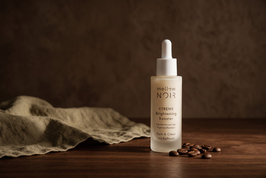 Produktaufnahme: mellow NOIR XTREME Brightening Booster in Milchglasflasche auf dunklem Holztisch mit Leinentuch und Kaffeebohnen